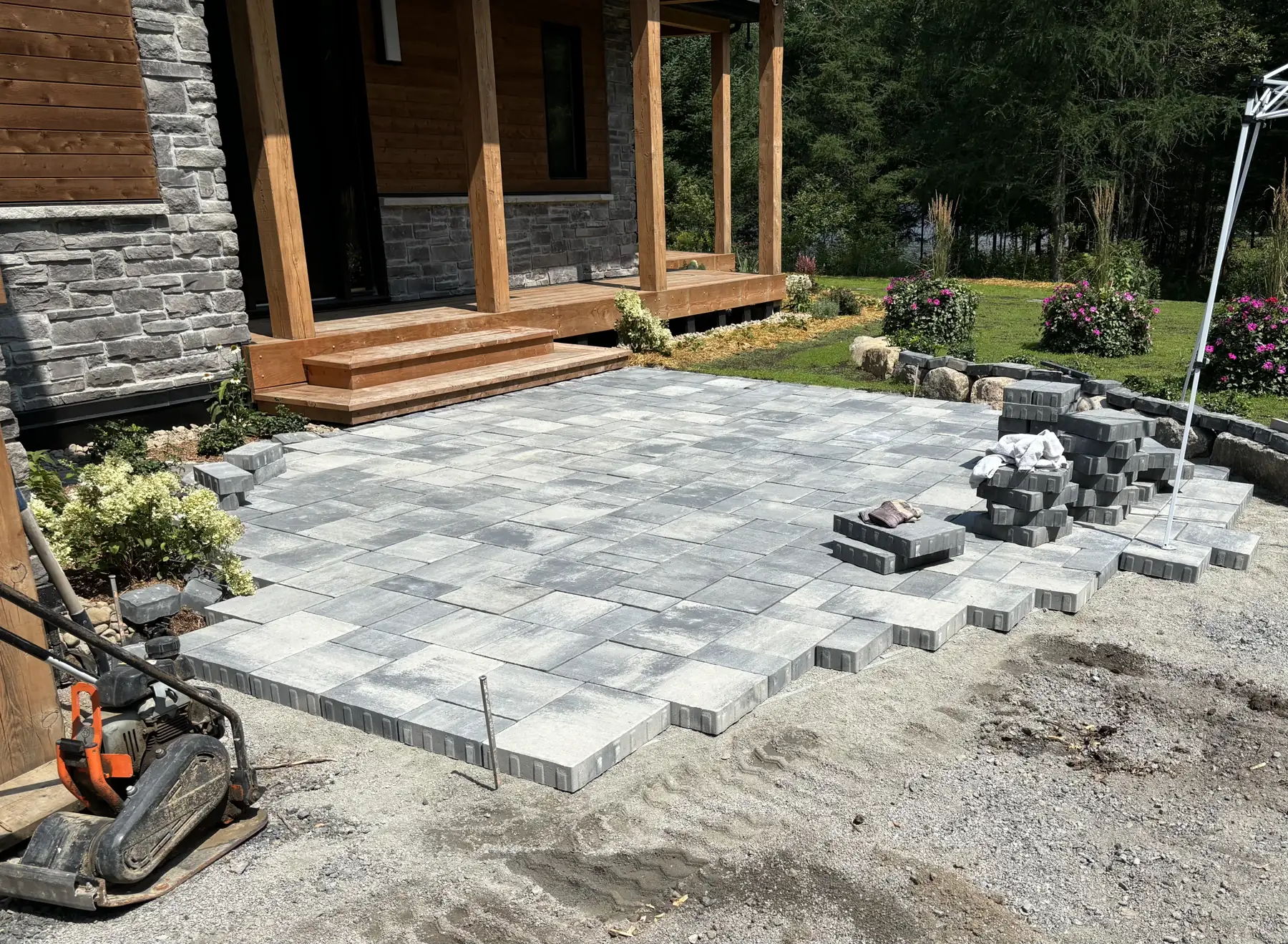 Pose de pavé de béton devant l'entrée d'une résidence : dalles posées, plaque vibrante et blocs empilés en attente